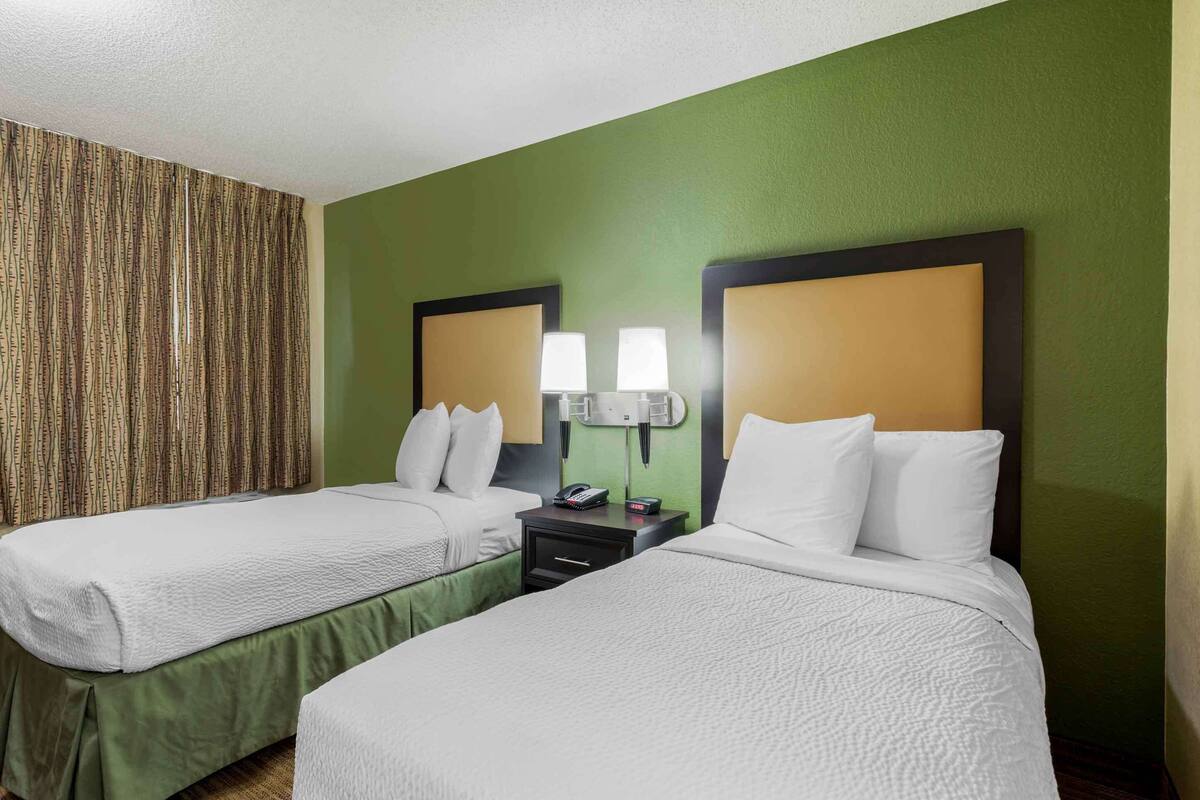 A hotel room with two beds, green walls, and a patterned curtain.