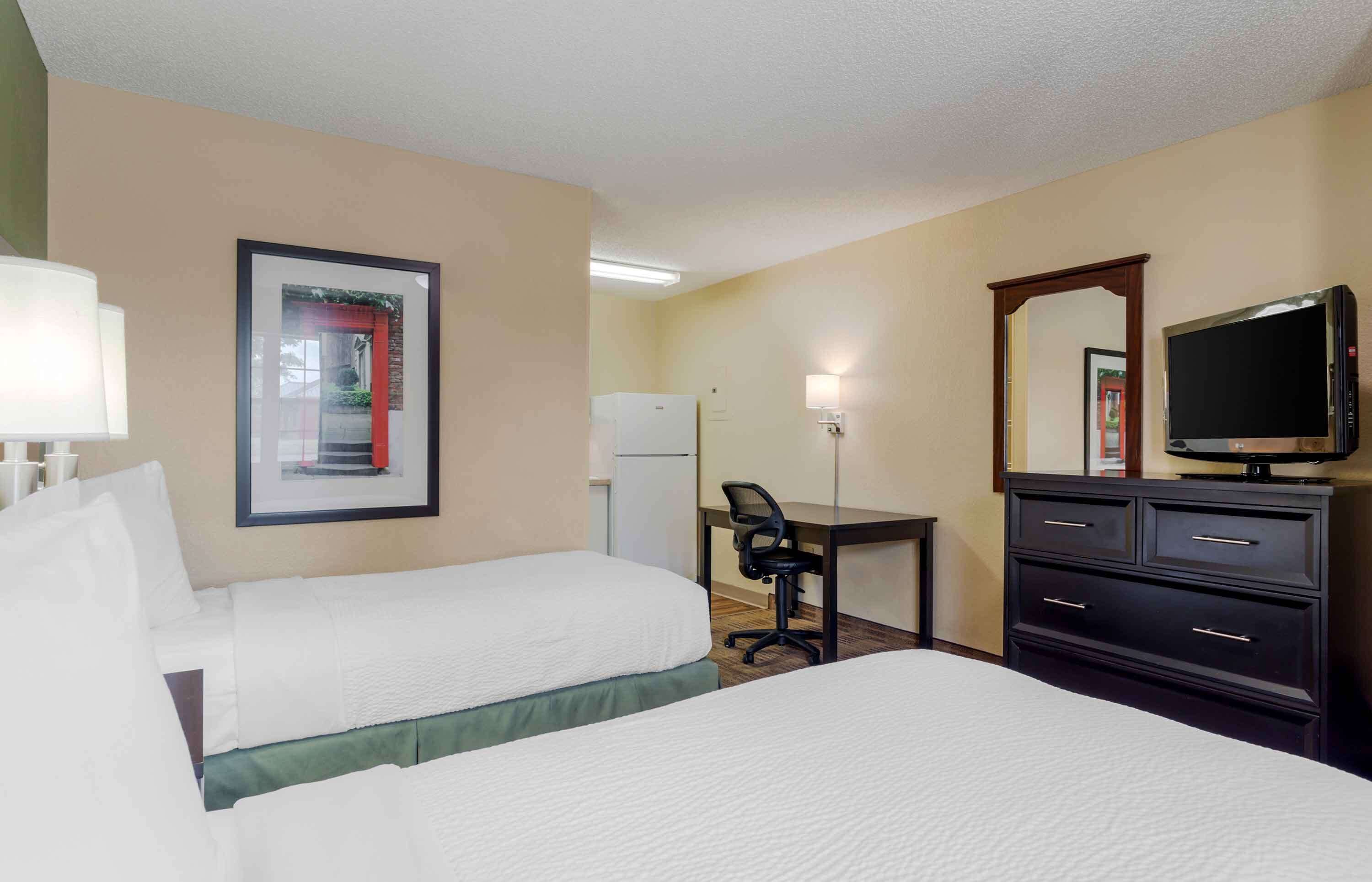 A hotel room with two beds, a desk with a chair, a television, a dresser, and a framed picture on the wall.