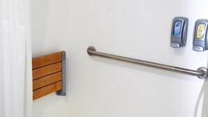 A shower area with a wooden bench, a grab bar, and two soap dispensers.