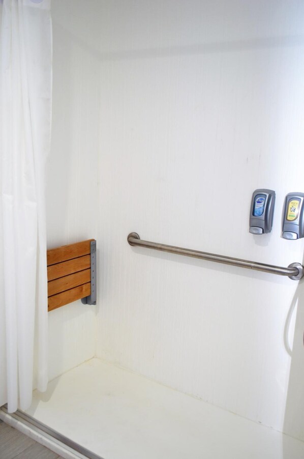 A shower area with a wooden bench, a grab bar, and two soap dispensers.