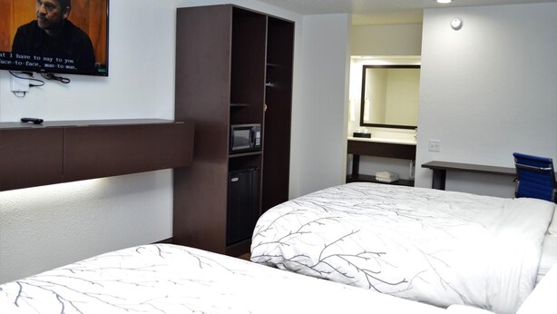 A hotel room with two beds, a television mounted on the wall, a wardrobe, a desk with a mirror, and a small kitchenette. - Athena Inn (Chattanooga)