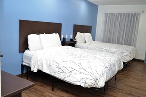 A hotel room with two beds, a desk, and a window with curtains.