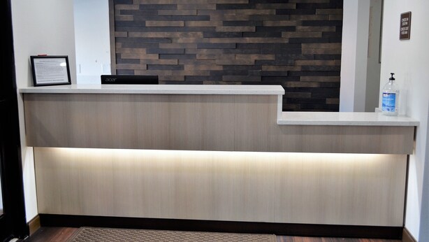 A reception desk with a wooden panel wall, a framed informational sign, and a bottle of hand sanitizer.