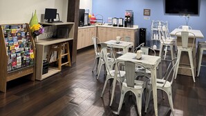 A room with a wooden floor, white chairs, a desk with a computer, a coffee machine, and a TV mounted on the wall.