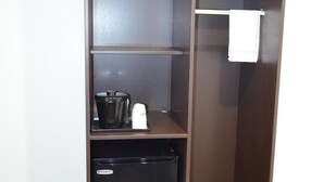 A room with a brown wardrobe, a small black refrigerator, and a trash bin.