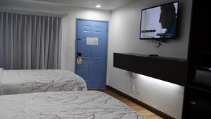 A hotel room with two beds, a TV mounted on the wall, a blue door, and a wooden floor.