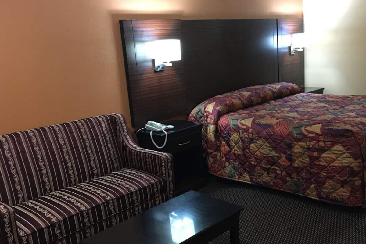 Ett hotellrum med en säng, en randig soffa, ett litet bord och ett nattduksbord med en telefon.
