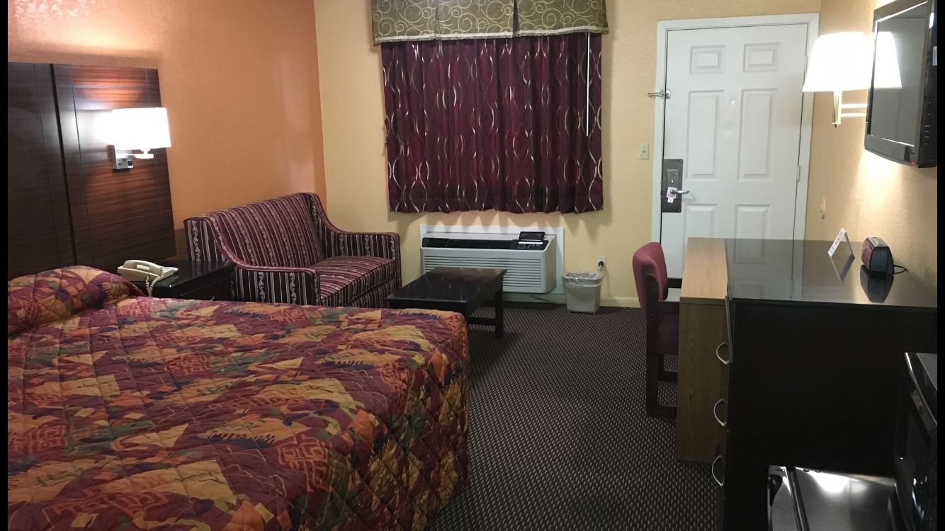 A hotel room with a large bed, a desk, a chair, a TV, and a window with curtains.