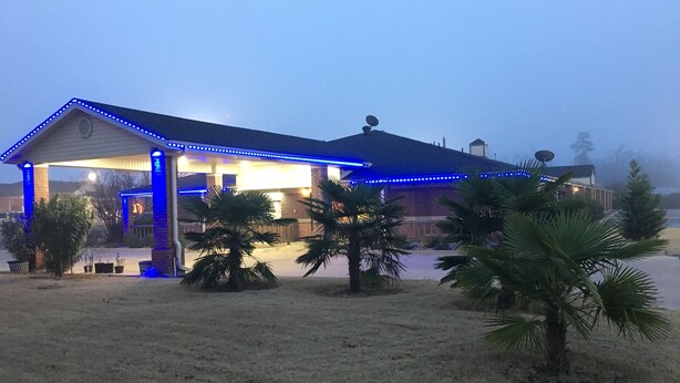 A building with a covered patio area, surrounded by palm trees and a grassy lawn. - Redwood Inn and Suites (White Hall)