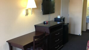 A hotel room with a desk, chair, TV, lamp, and a trash bin. - Redwood Inn and Suites (White Hall)