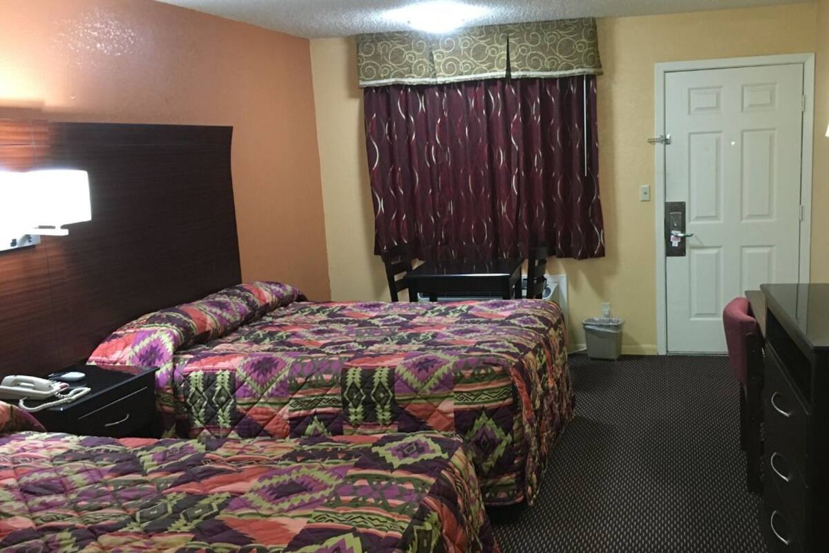 Ett hotellrum med två sängar, ett skrivbord, en stol, en TV, en byrå och en dörr.