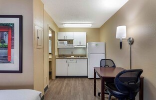 Habitación de hotel compacta con kitchenette, comedor con mesa y sillas, y una cama.