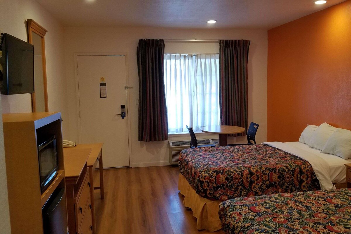 A hotel room with two beds, a desk, a chair, and a television.