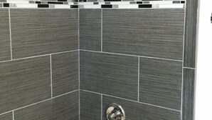 A shower with a curved showerhead, a white bathtub, and a tiled wall with a black and white accent strip. - Rodeway Inn Alameda-Oakland (Alameda)