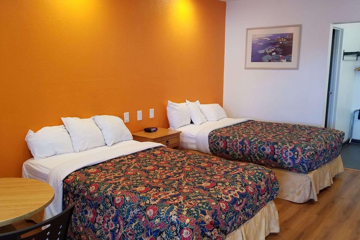 A hotel room with two beds, a small table, and a chair.