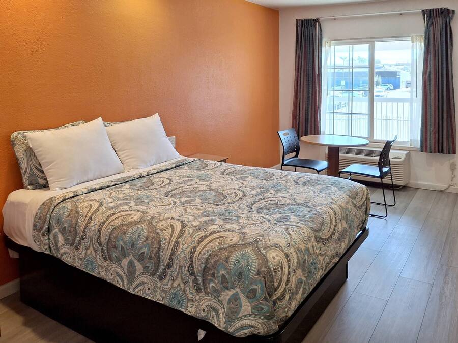 A hotel room with a bed, a small table, two chairs, and a window with curtains.