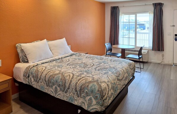 Habitación de hotel con cama, una mesita, dos sillas y una ventana con cortinas.