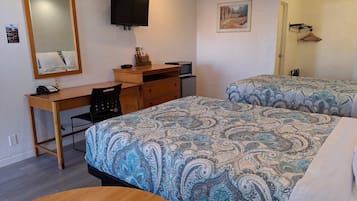 A hotel room with a desk, two beds with patterned bedding, a television, a mirror, and a door with a coat rack.