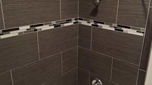 A corner of a room with dark brown tiled walls and a small, circular drain in the center. - Rodeway Inn Alameda-Oakland (Alameda)