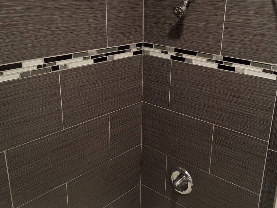 A corner of a room with dark brown tiled walls and a small, circular drain in the center.