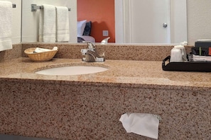 Un baño con encimera de granito, lavamanos, espejo y toallero.