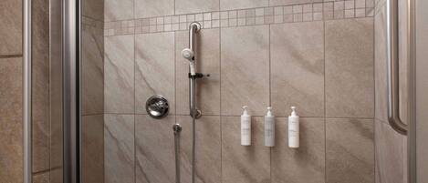 A shower area with a handheld showerhead, a wall-mounted faucet, and two bottles of shampoo.