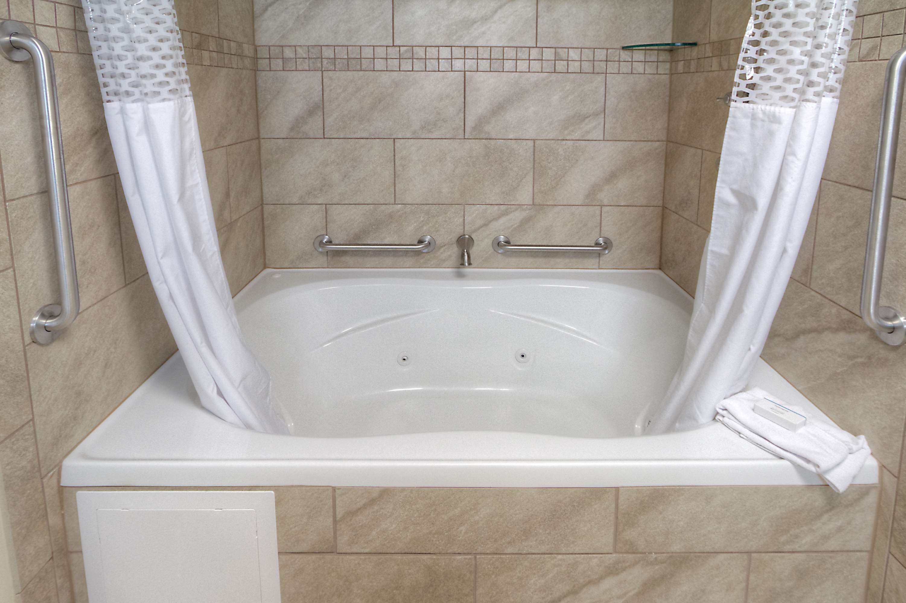A white bathtub with grab bars, a shower curtain, and a towel on the side.