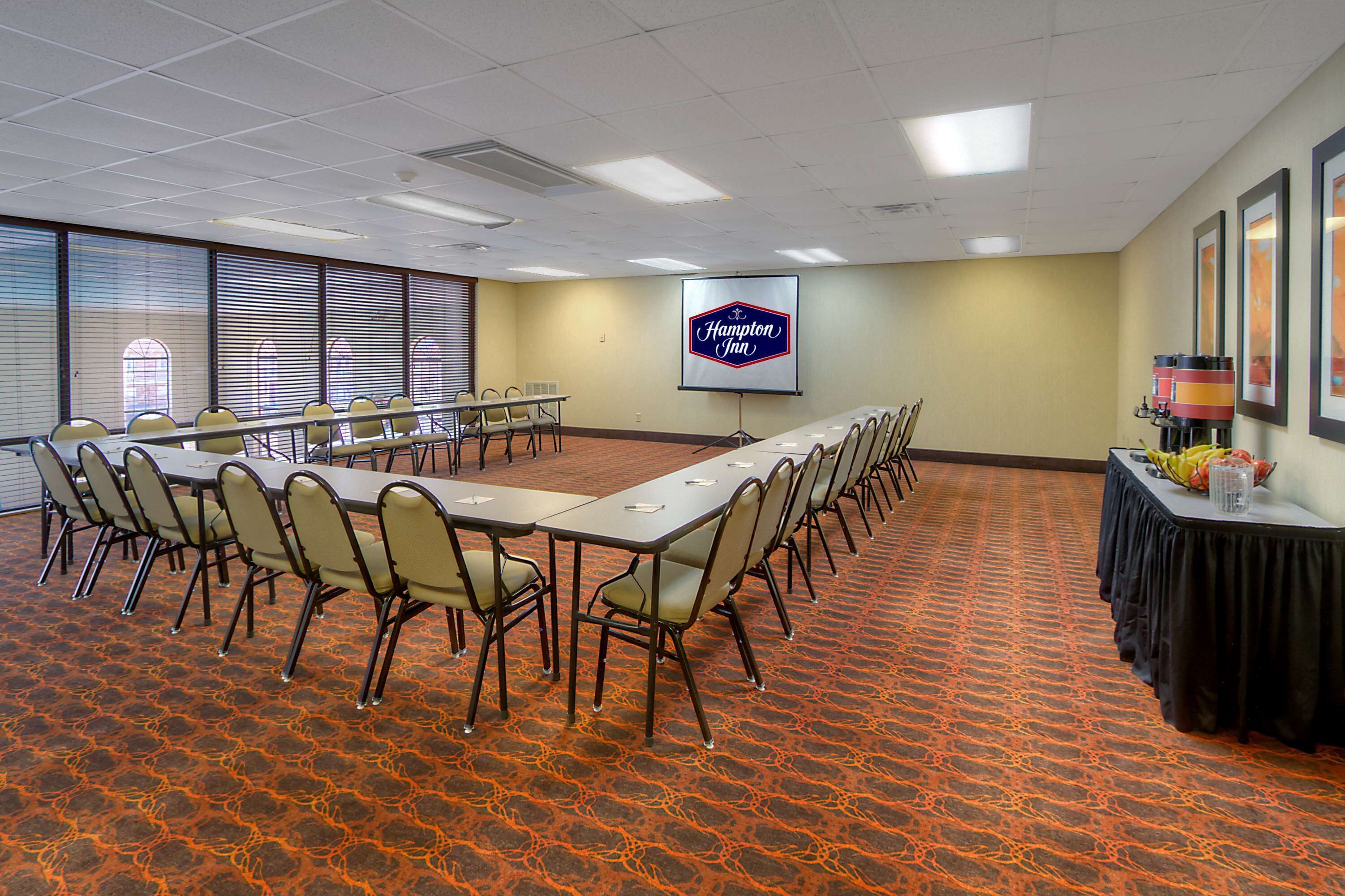 A conference room with a long table, chairs, a projector screen, and a Hampton Inn logo.