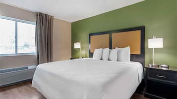 A hotel room with a large bed, two bedside tables with lamps, a window with curtains, and a green wall.