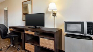 Una camera d'albergo con una scrivania, una televisione, un forno a microonde, un frigorifero, una sedia e una lampada.