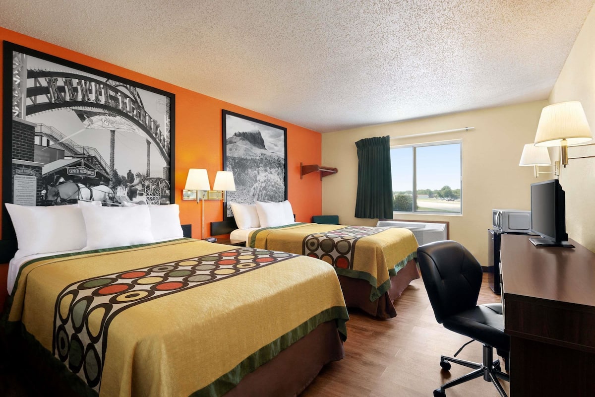 A hotel room with two beds, a desk, a chair, a television, and a window with curtains.