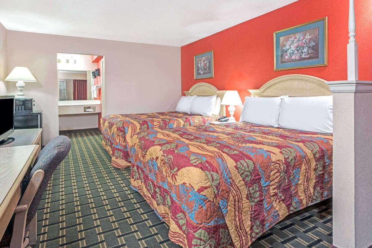 Ein Hotelzimmer mit einem großen Bett, einem Schreibtisch mit Stuhl, einem Spiegel und einem Fernseher.