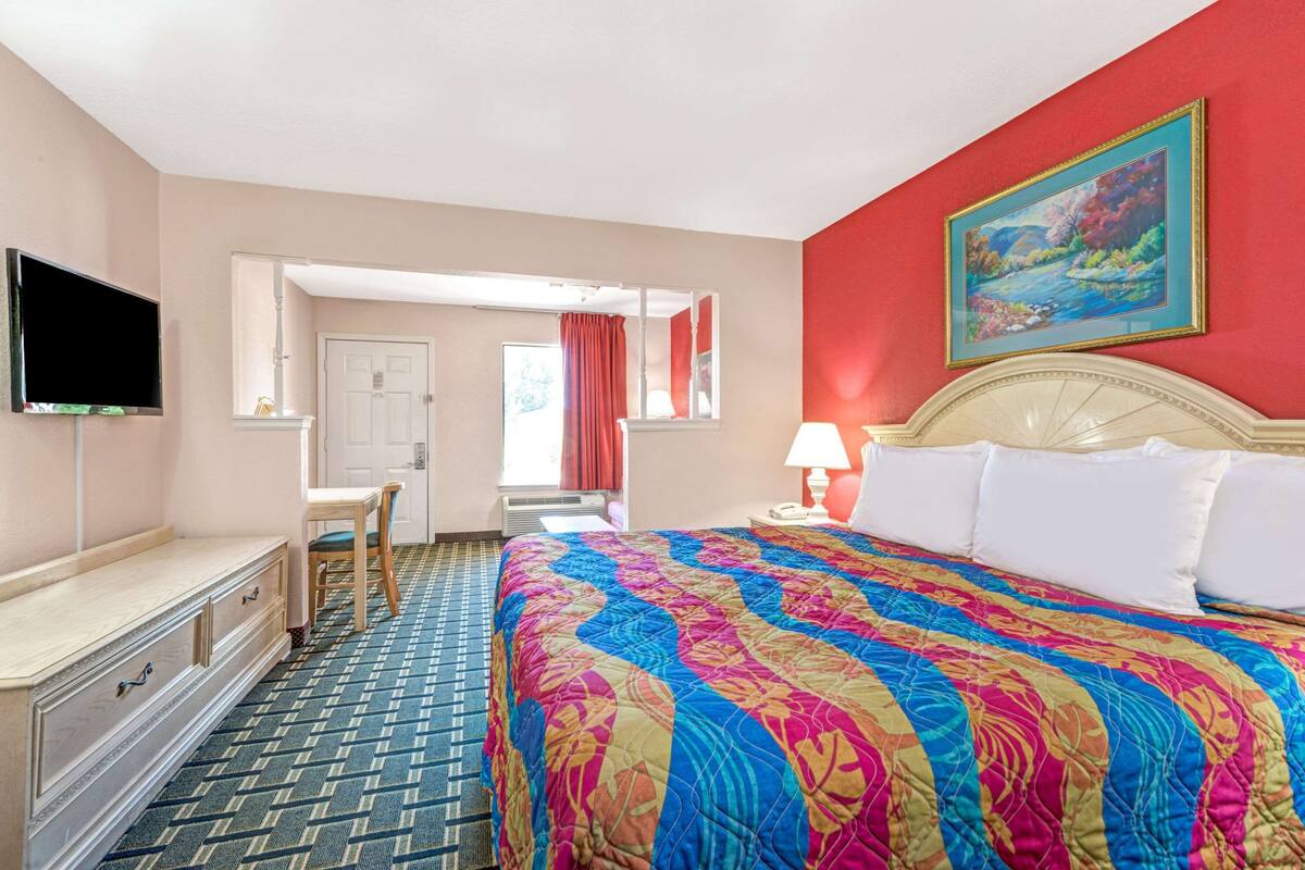 Ein Hotelzimmer mit einem großen Bett, einem Schreibtisch, einem Fernseher und einem Bild an der Wand.