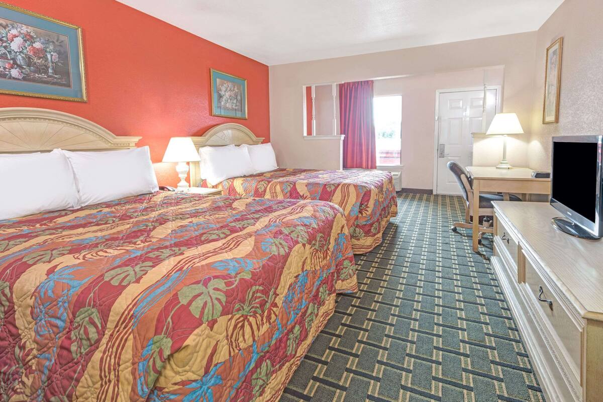 Ein Hotelzimmer mit zwei Betten, einem Fernseher, einem Schreibtisch und einem Sessel.