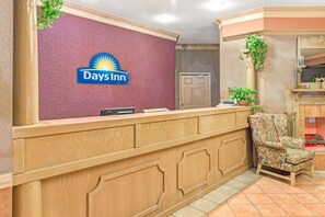 Una recepción con el letrero de Days Inn, una barra de madera, un sillón floral y una puerta al fondo.