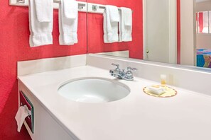 Un baño con un lavabo blanco, dos grifos y un espejo. Hay toallas blancas colgadas en un perchero sobre el lavabo.