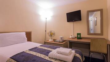 A hotel room with a bed, a desk with a flat-screen TV, a fan, and a chair.