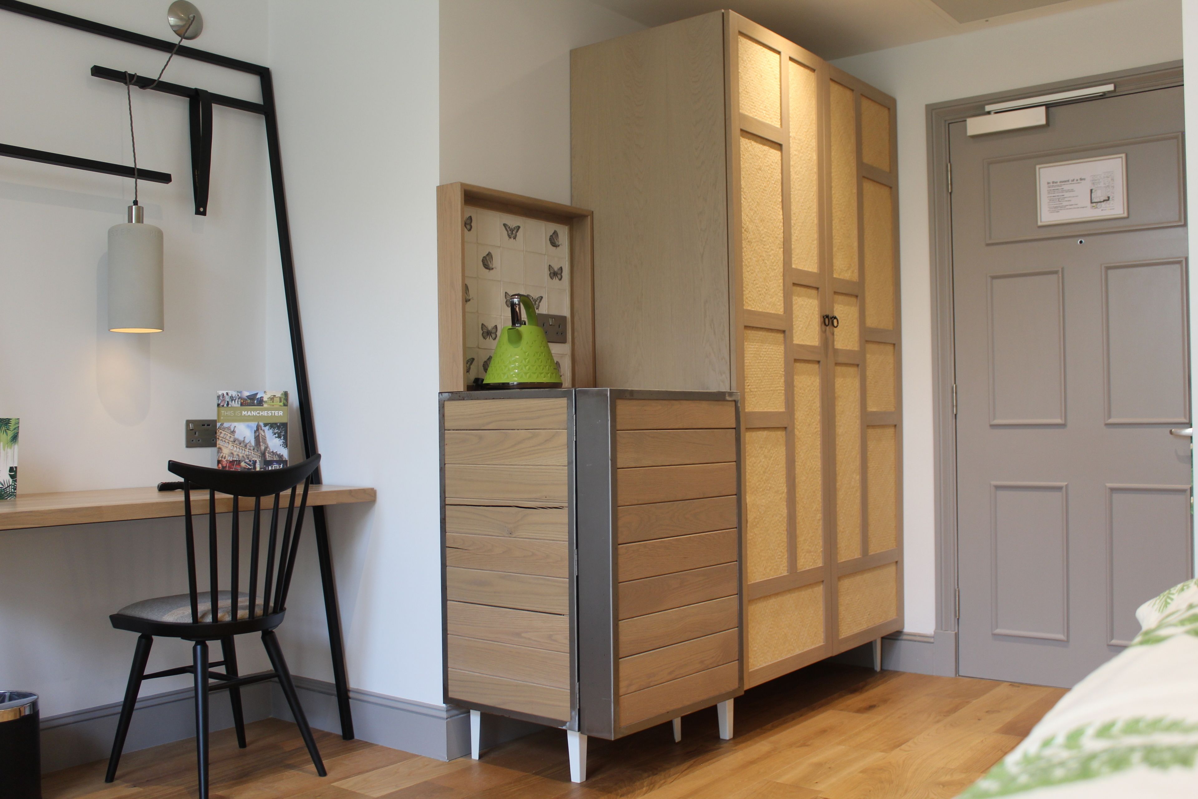 A bedroom with a wooden wardrobe, a desk with a chair, and a bed with a green and white bedspread.