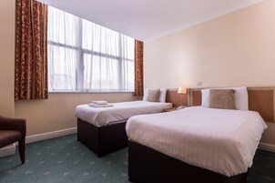 Habitación de hotel con dos camas, una silla y un ventanal con cortinas.