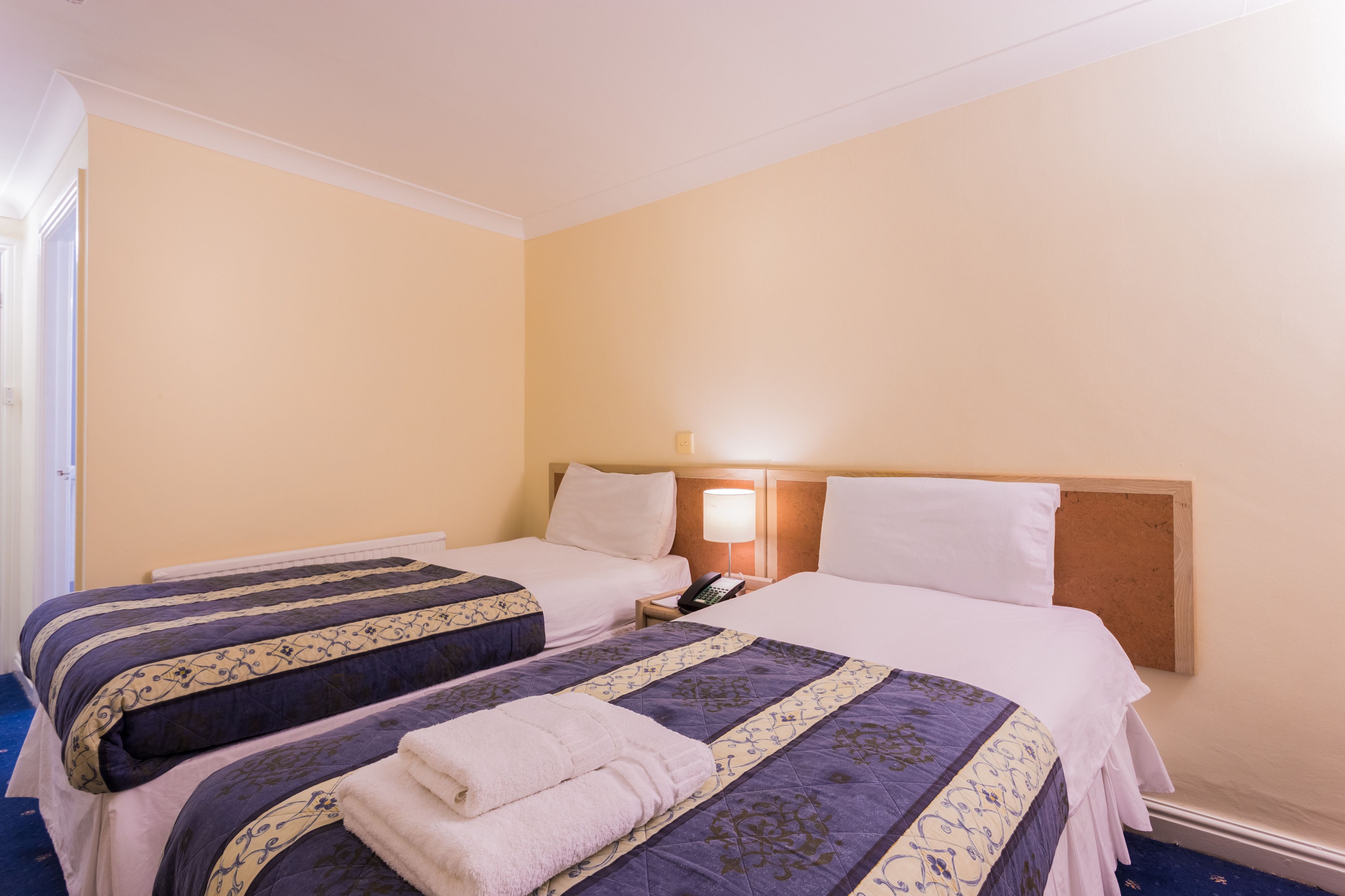 Una habitación de hotel con dos camas, una mesita de noche con lámpara y un cabecero de madera.