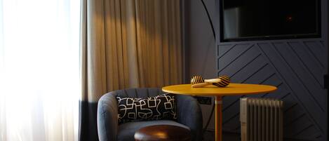 A modern room with a blue armchair, a small round table with a brush, a black floor lamp, a radiator, and a TV mounted on the wall.