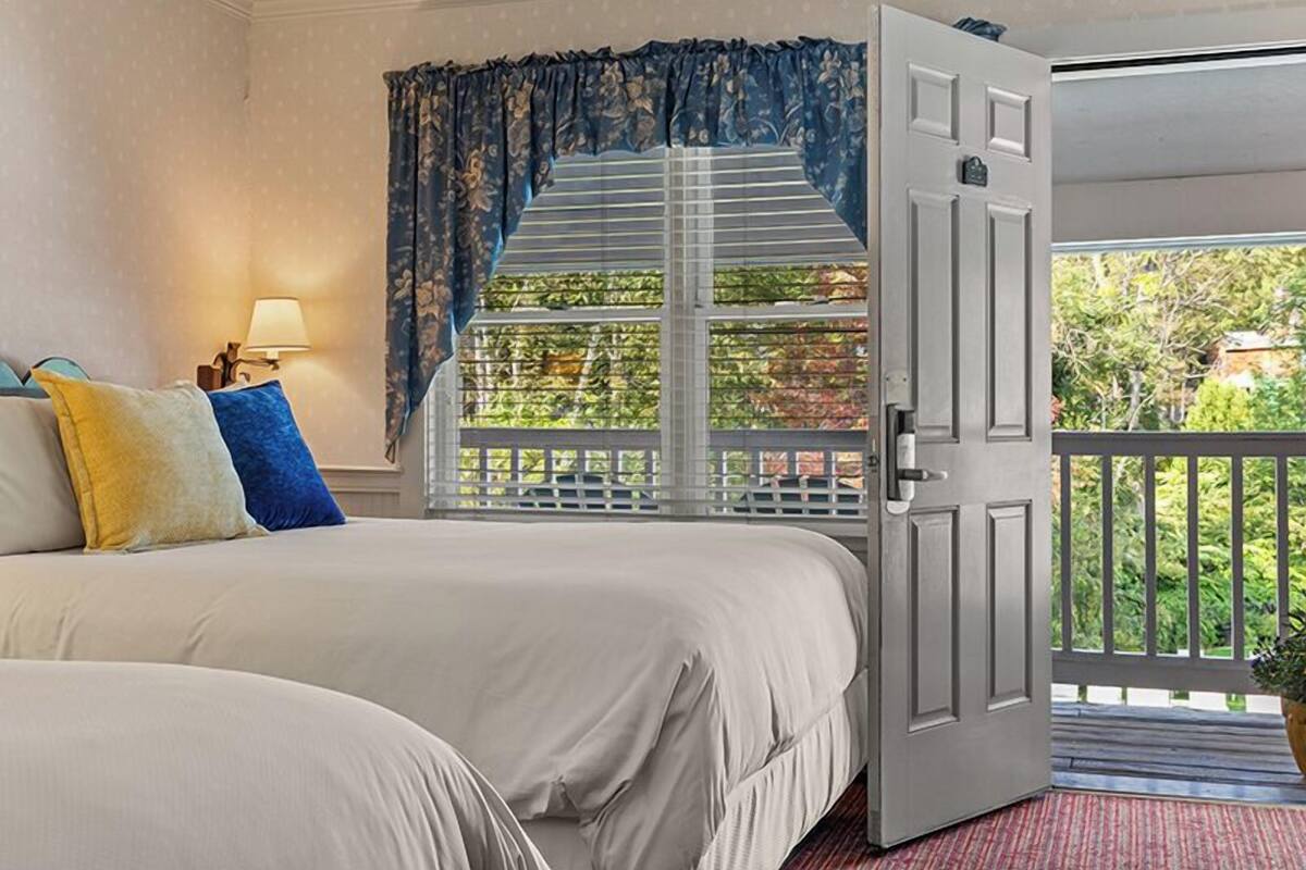 A bedroom with a large bed, a window with a view of greenery, and a door leading to an outdoor balcony.
