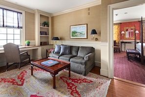 A living room with a sofa, a coffee table, a desk, and a bookshelf.