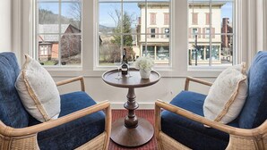 A room with two wicker chairs, a round wooden table, and a view through large windows. - Green Mountain Inn (Stowe)