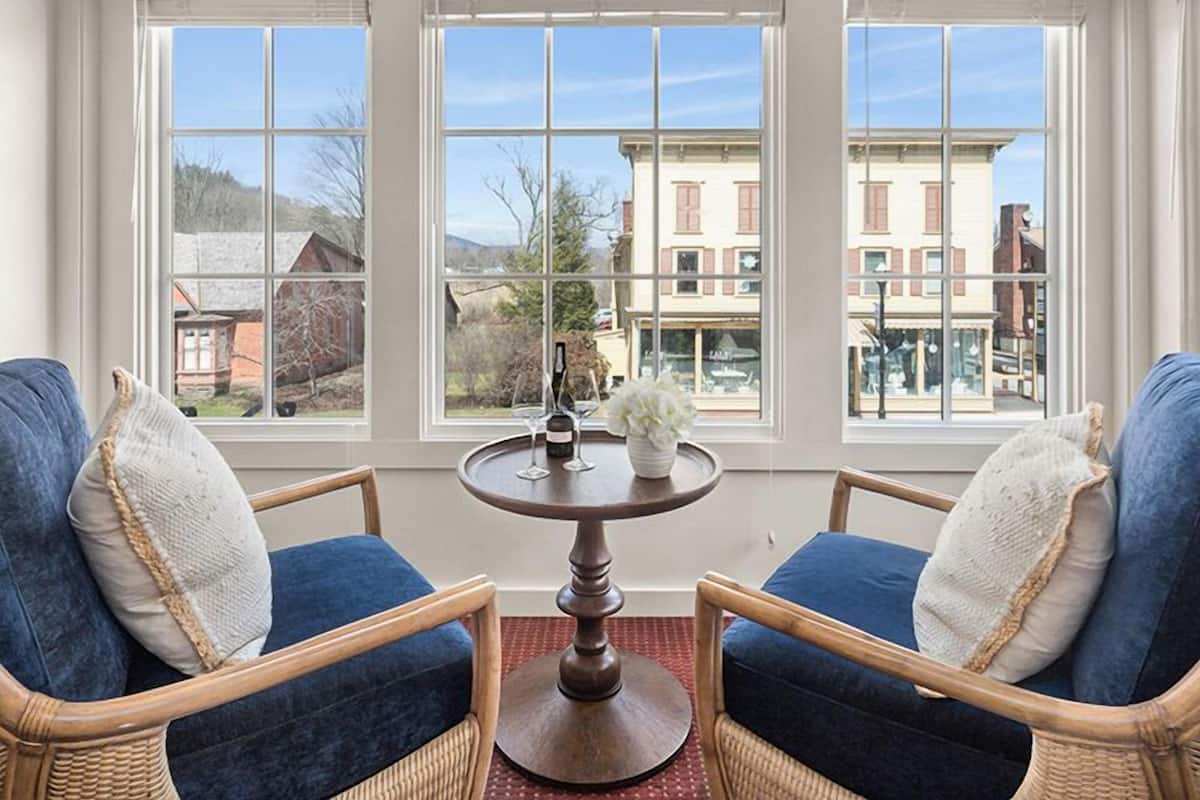 A room with two wicker chairs, a round wooden table, and a view through large windows.