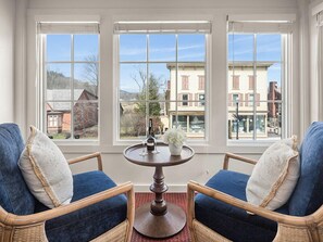 A room with two wicker chairs, a round wooden table, and a view through large windows. - Green Mountain Inn (Stowe)