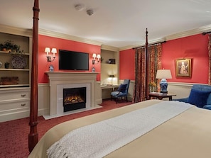A hotel room with a fireplace, a television, a desk with a chair, and a bed.