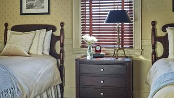 A bedroom with two beds, a nightstand with a lamp, a vase with flowers, and a clock.