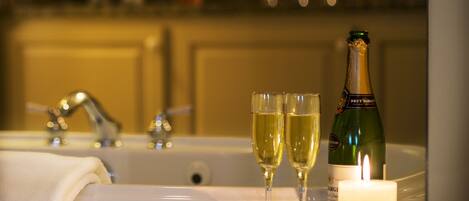 A bathroom with a bathtub, two glasses of champagne, a bottle of Brut Dargies wine, and a lit candle.