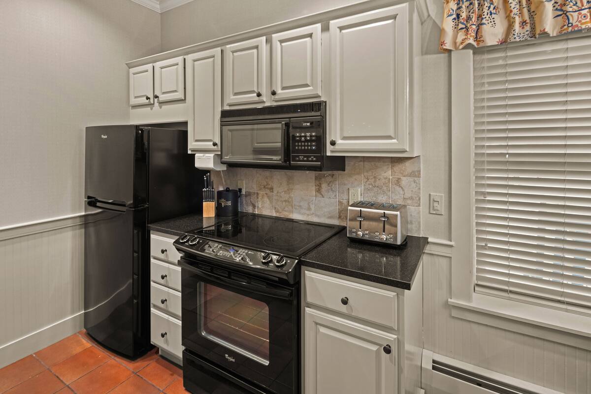A kitchen with white cabinets, a black refrigerator, a microwave, a stove, and a toaster.